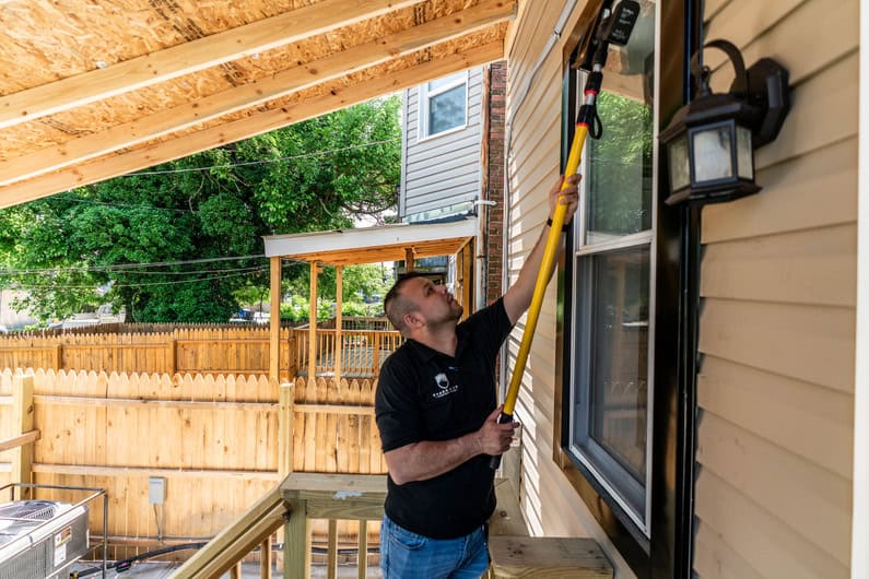 Home inspector checking window for lead paint hazards outside house.